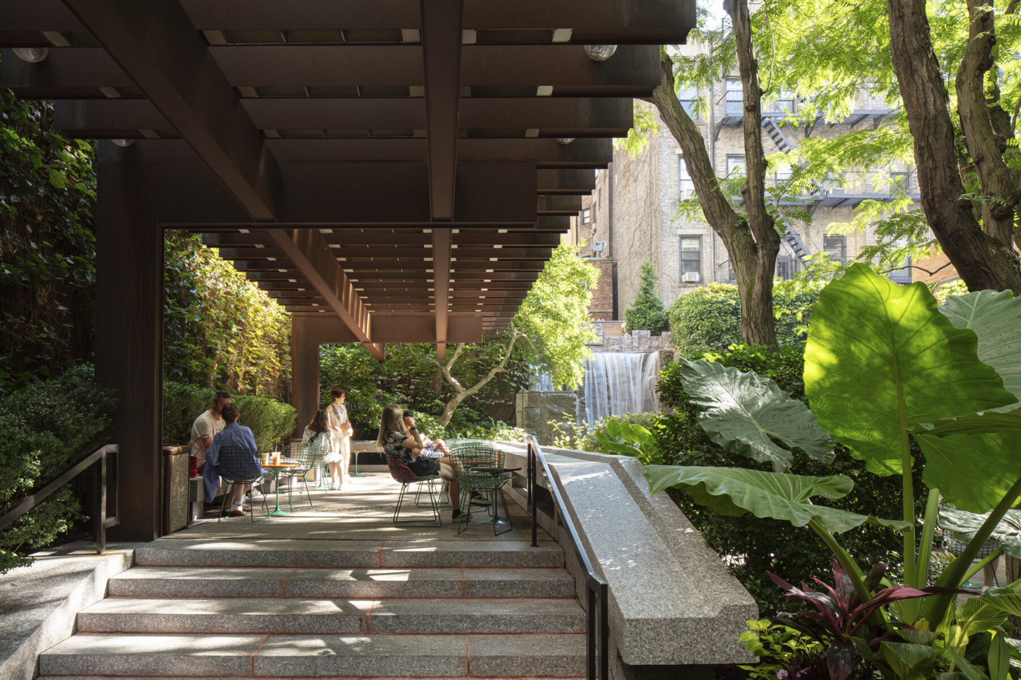 View looking up staircase framed by overhanging trellis and park visitors sitting at tables in the sunlight