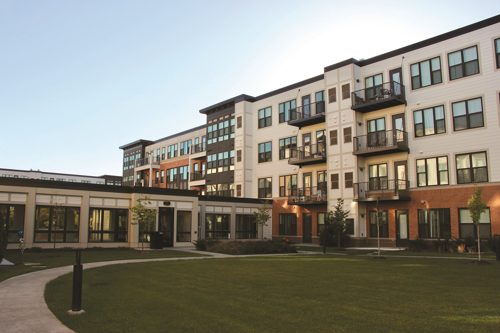 Exterior of amodern 4-story residential building with balconies, a sprawling lawn and no visible HVAC units