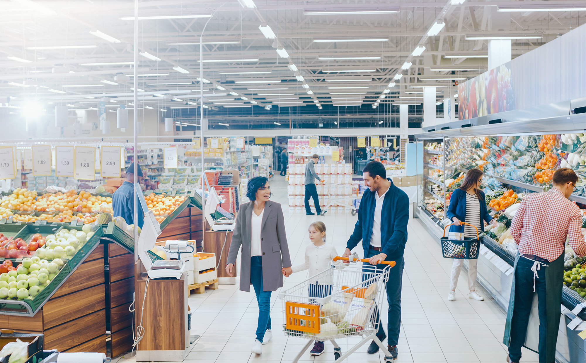 At the Supermarket: Happy Family of Three, Holding Hands, Walks Through Fresh Produce Section of the Store. Father, Mother and Daughter Having Fun Time Shopping. High Angle Panoramic Shot.