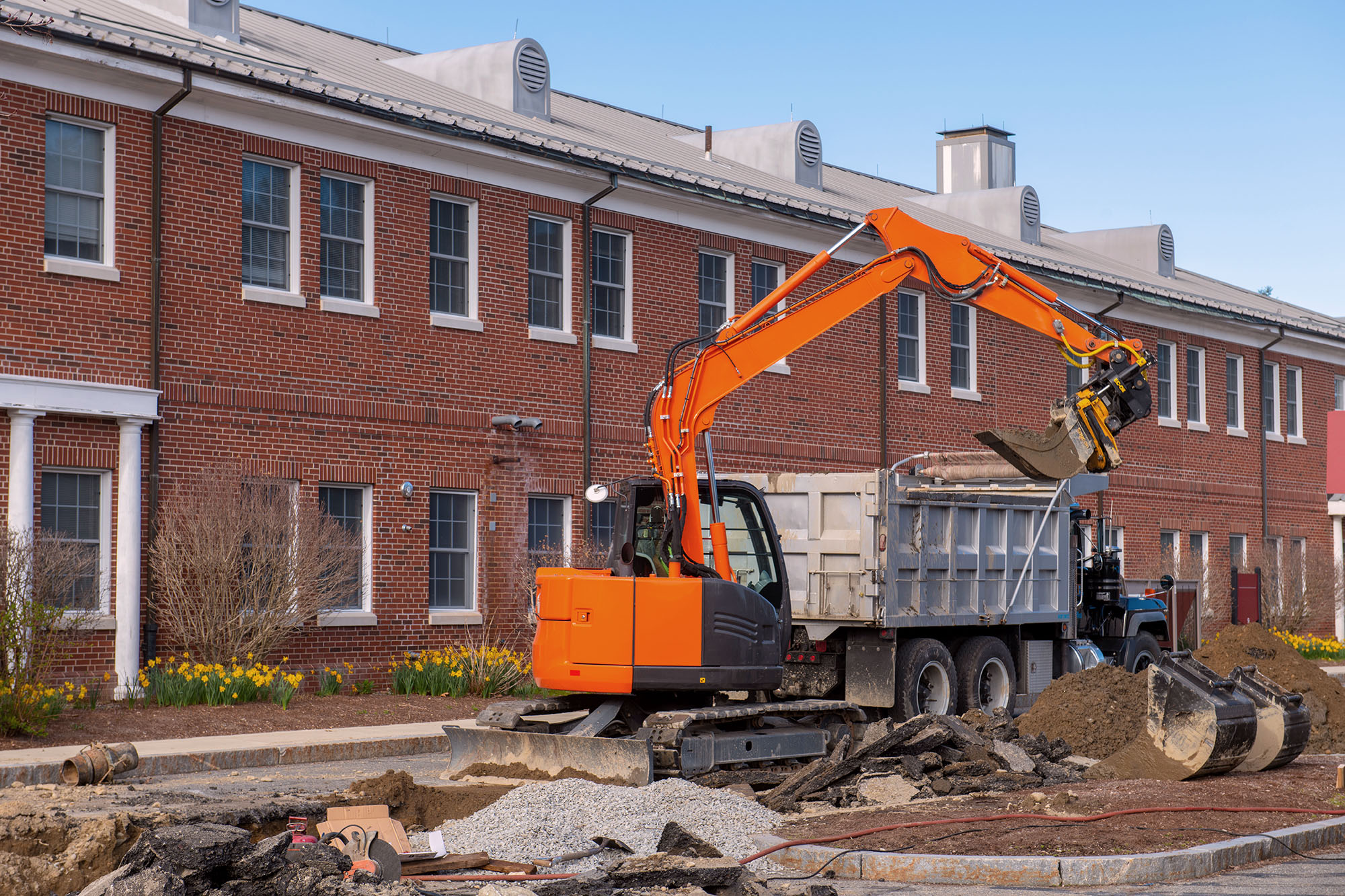 Excavator digging a trench and loading on the dump truck in Middlesex Community College in town of Bedford, Massachusetts MA, USA