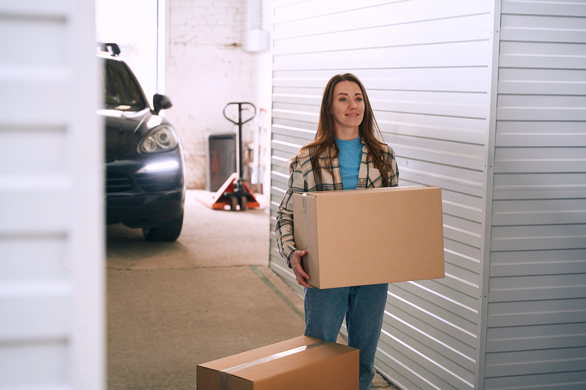 Young lady with big cardboard boxes into warehouse with self-storage unit