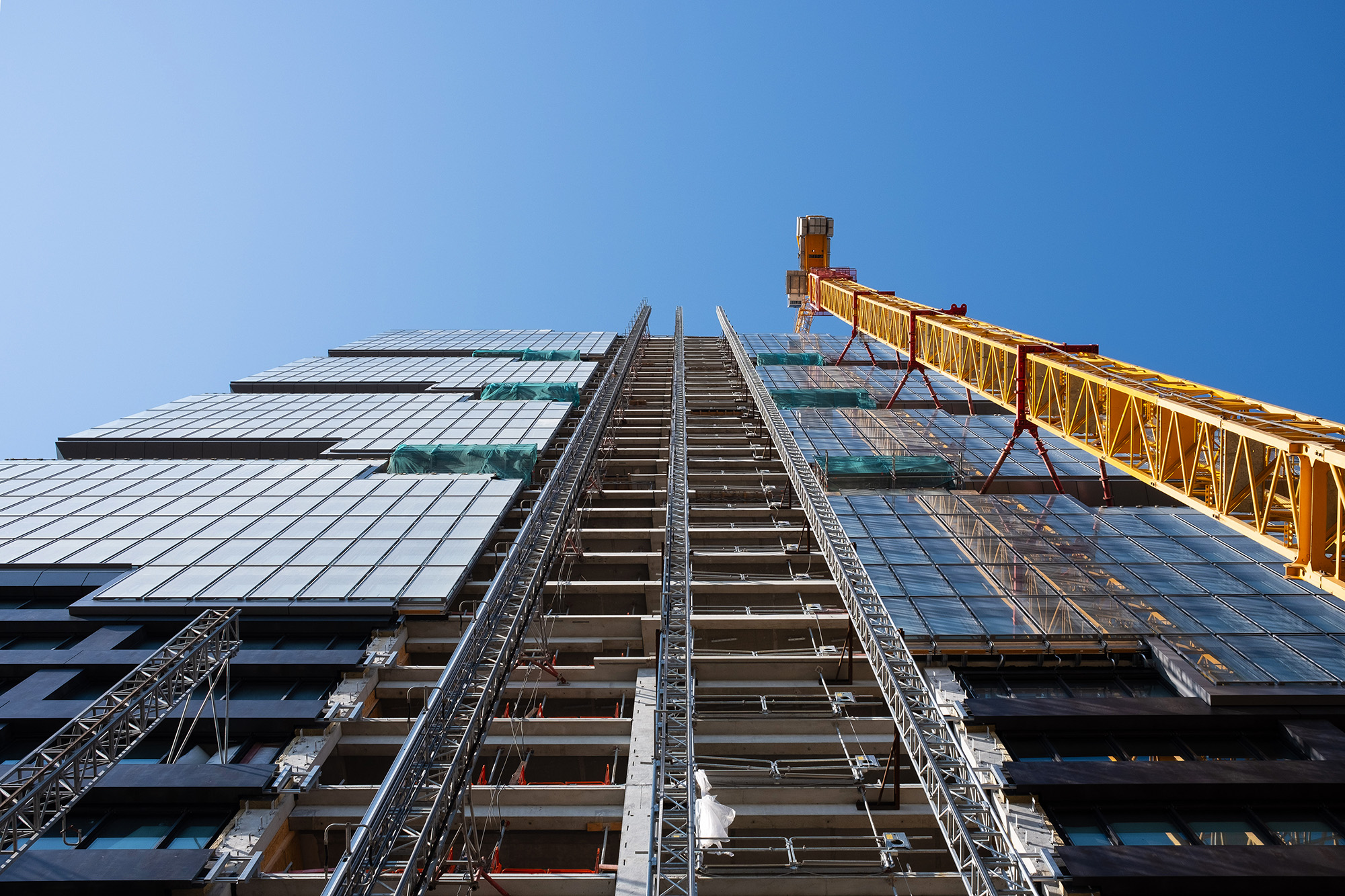 Looking up at the construction site of a skyscraper building with a yellow crane an an exterior elevator