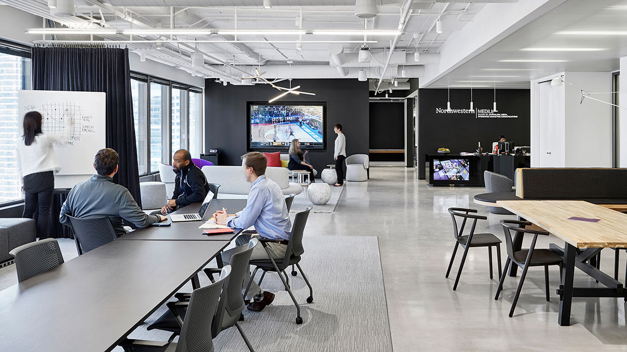 A group of people sitting at tables in a room with a large screen.