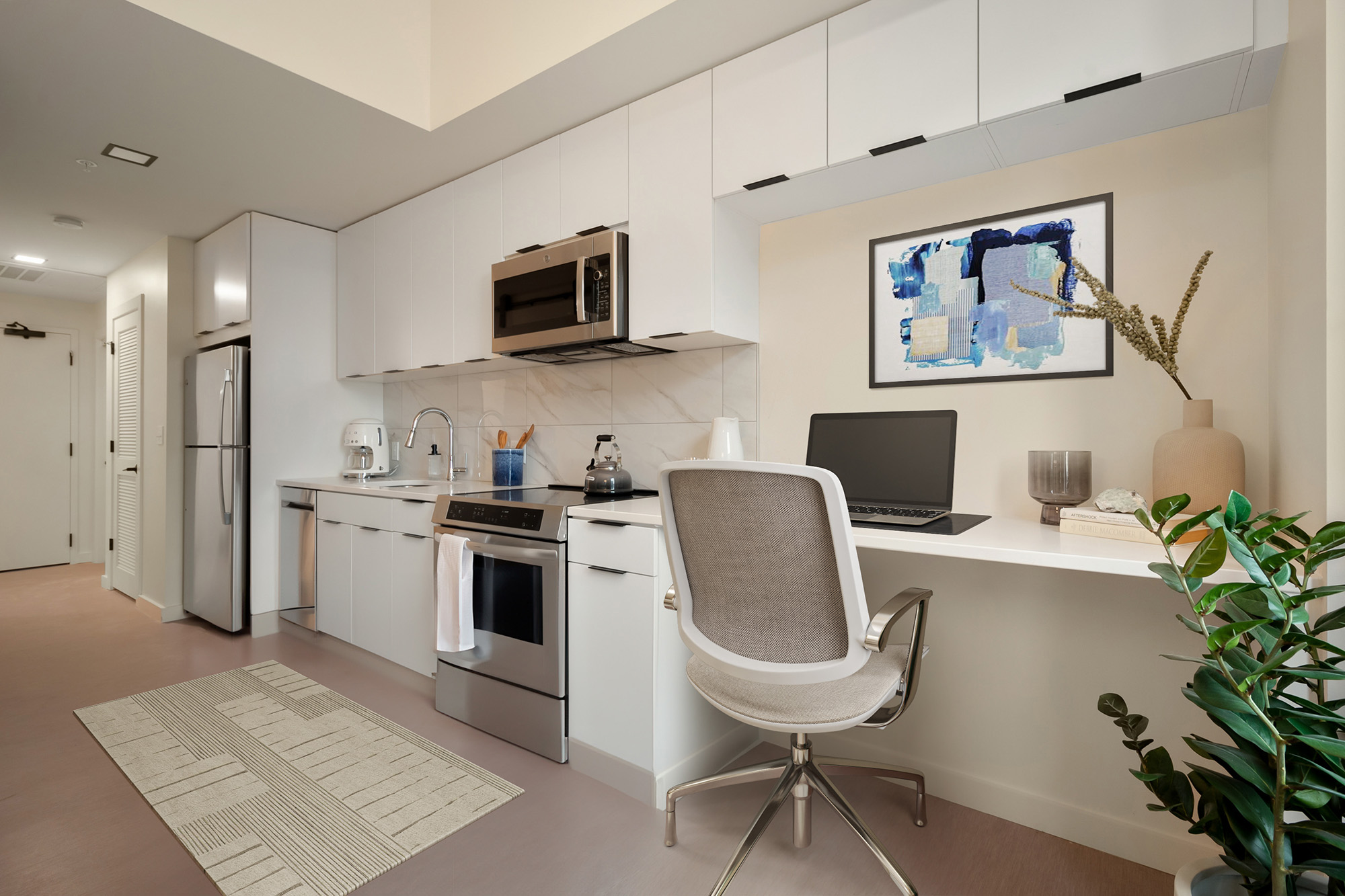 Micro-unit interior featuring a desk, compact appliances, and overhead storage